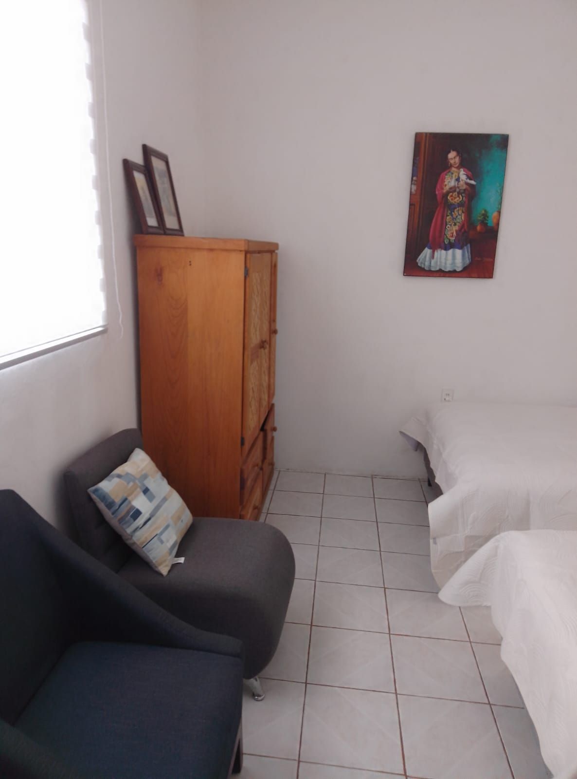 Una habitación con un armario de madera, dos camas, una silla y un cuadro en la pared.