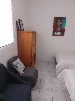 Una habitación con un armario de madera, dos camas, una silla y un cuadro en la pared.