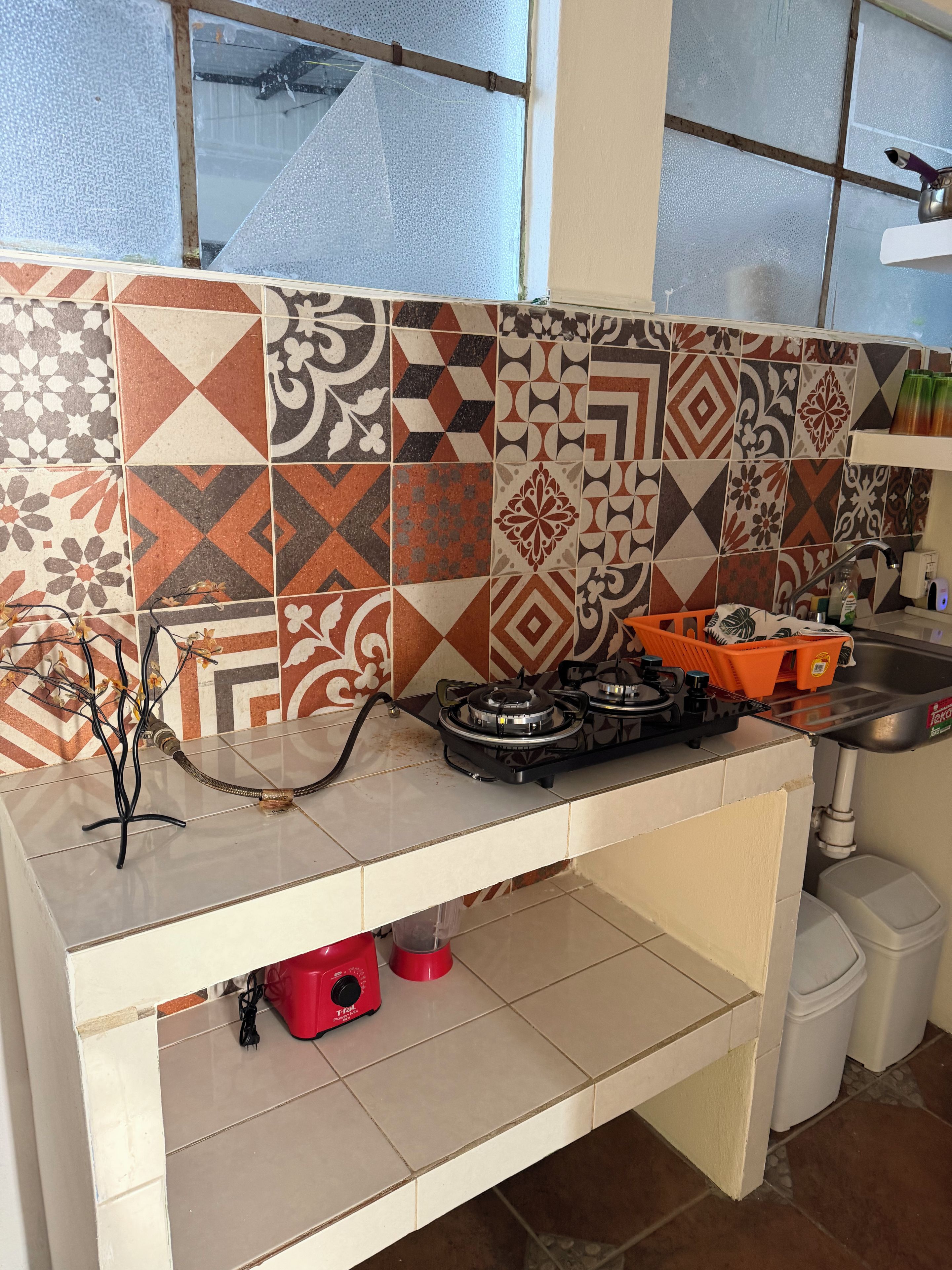 Une cuisine équipée d’une cuisinière à gaz, d’un évier et d’un plan de travail recouvert de carreaux.