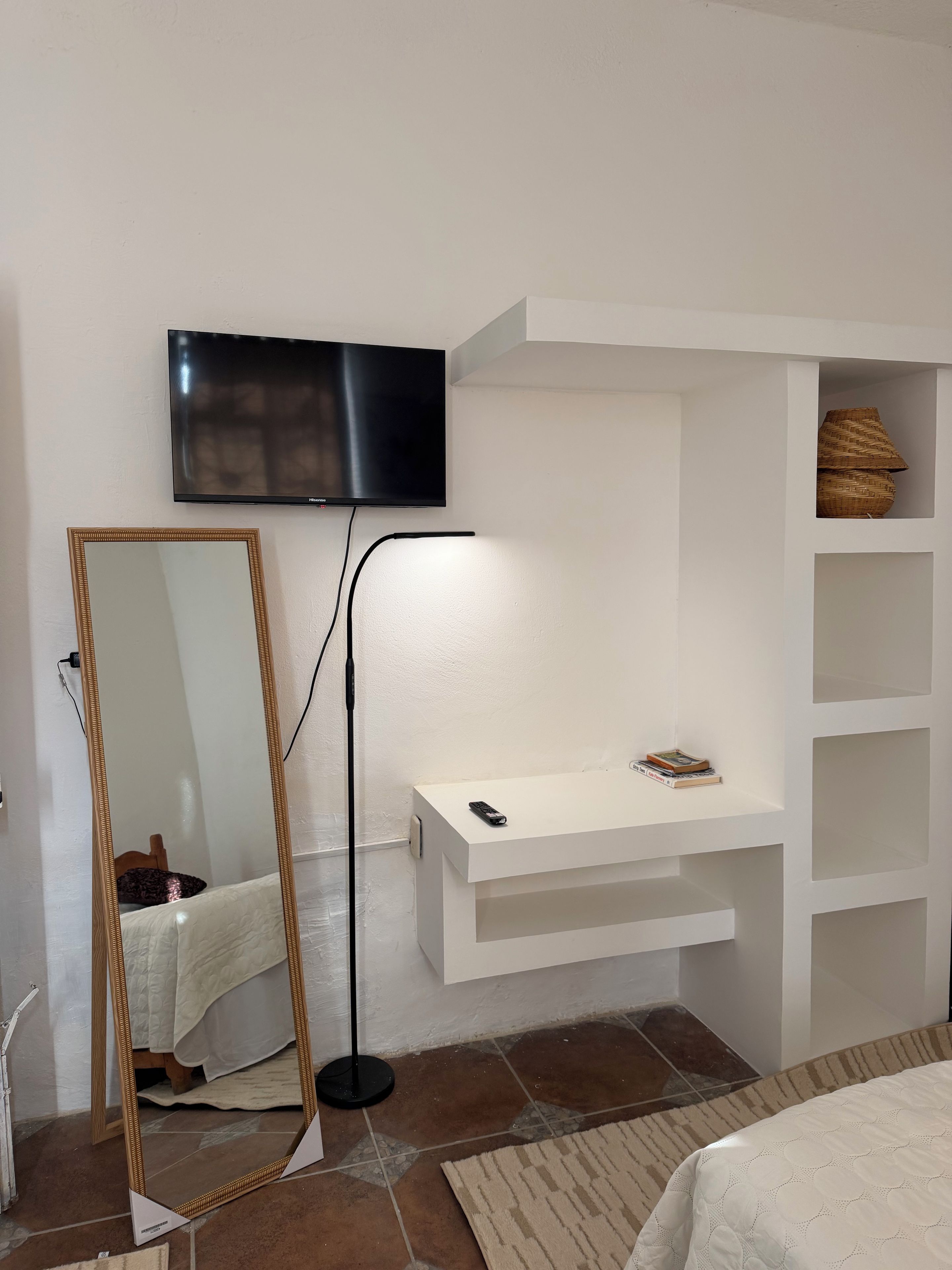 A bedroom with a bed, a bedside table, a TV mounted on the wall, and a mirror.