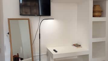 A bedroom with a bed, a bedside table, a TV mounted on the wall, and a mirror.