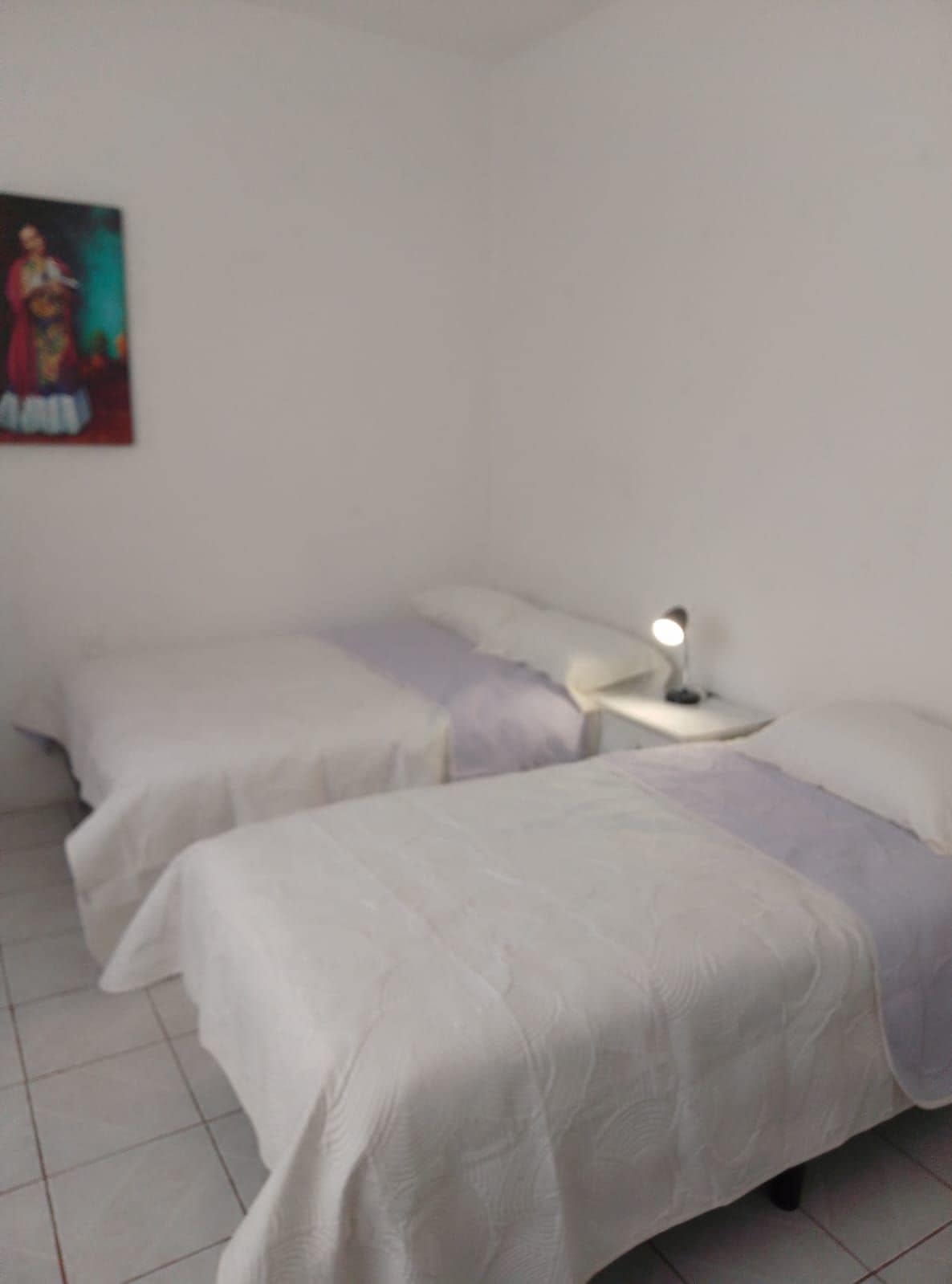Quarto com duas camas, mesa de cabeceira com abajur e um quadro pendurado na parede.