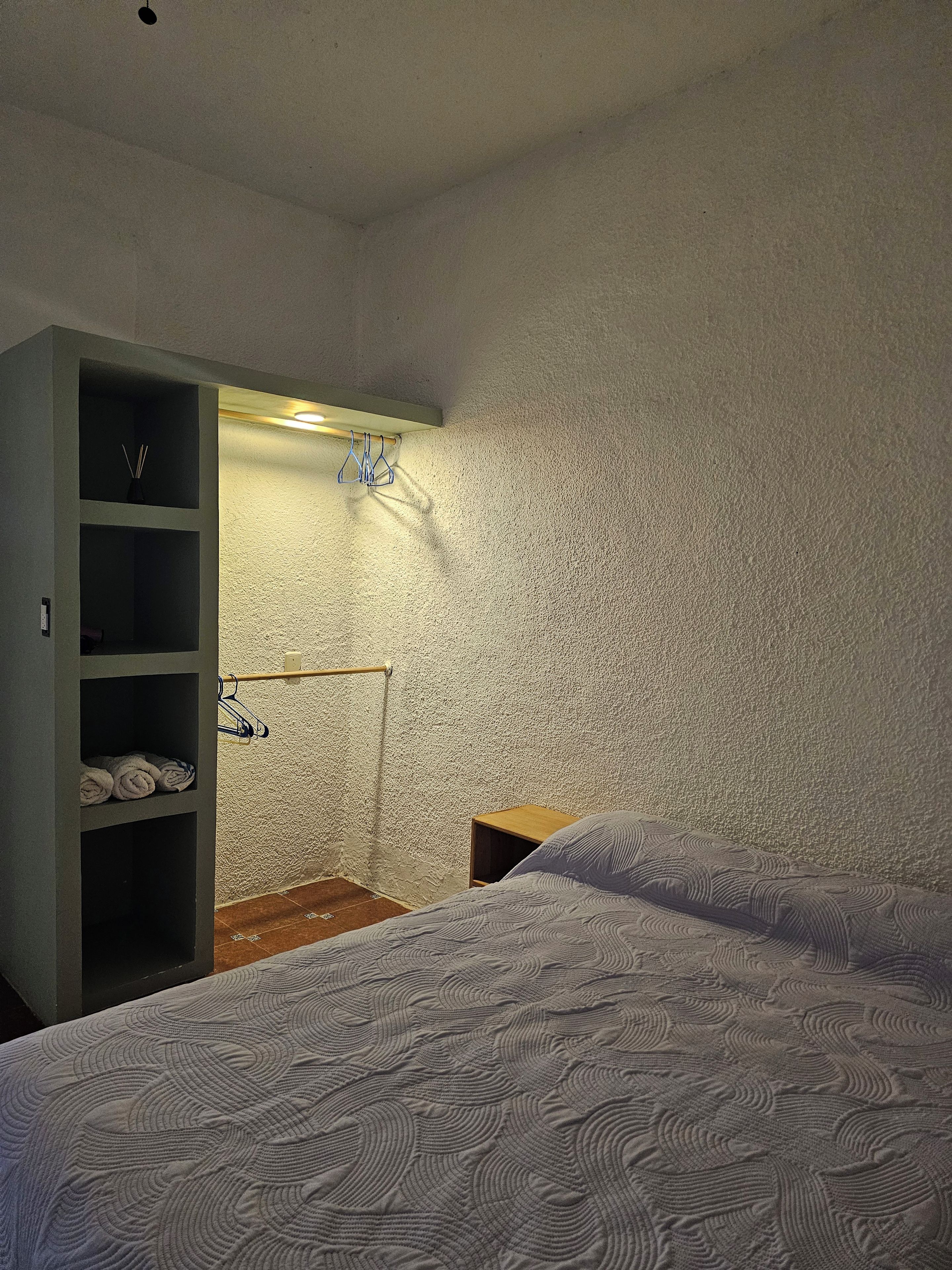 A bedroom with two beds, a wardrobe, and a shelf unit with towels.
