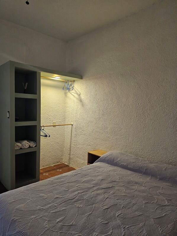 A bedroom with two beds, a wardrobe, and a shelf unit with towels.