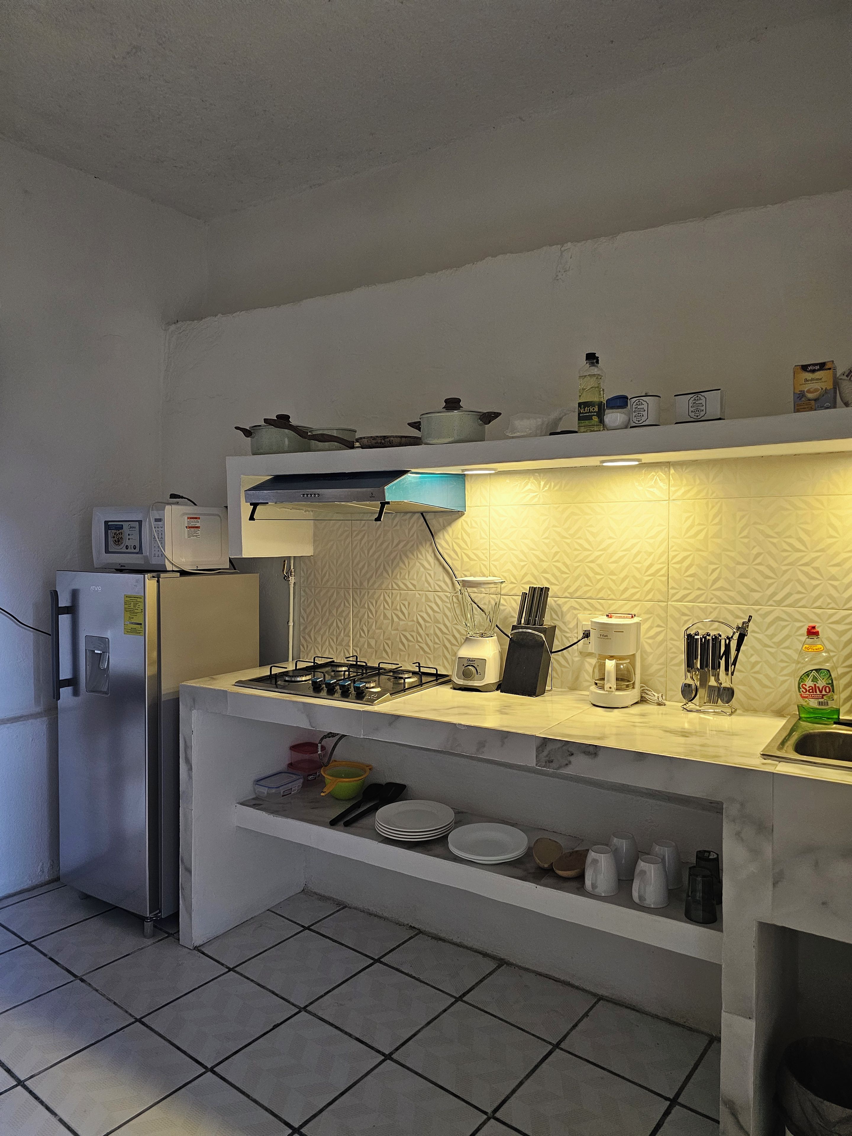 Cocina compacta equipada con refrigerador, estufa, microondas y varios utensilios de cocina.