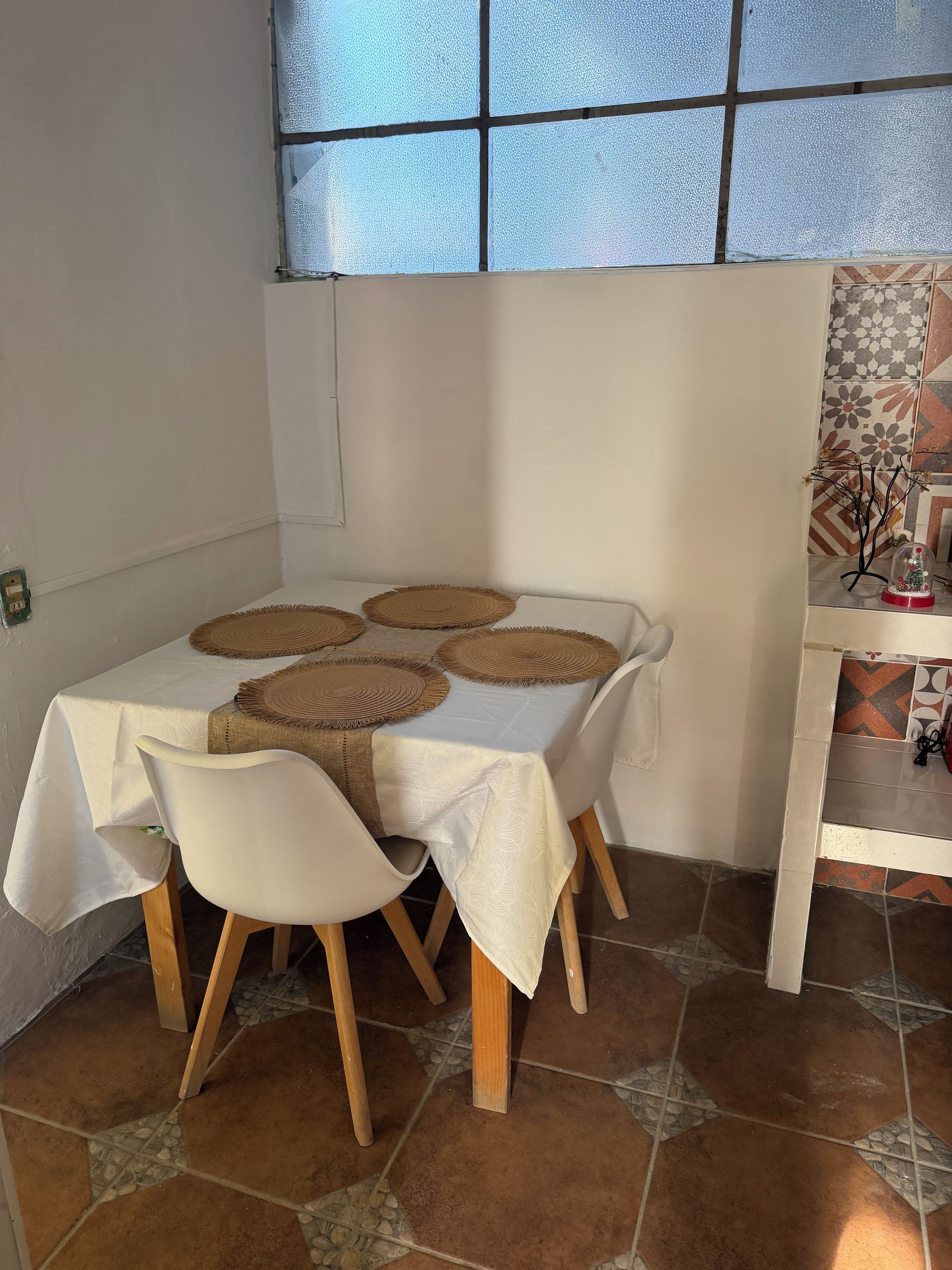 Comedor con una mesa dispuesta para cuatro personas, con individuales tejidos y sillas blancas.