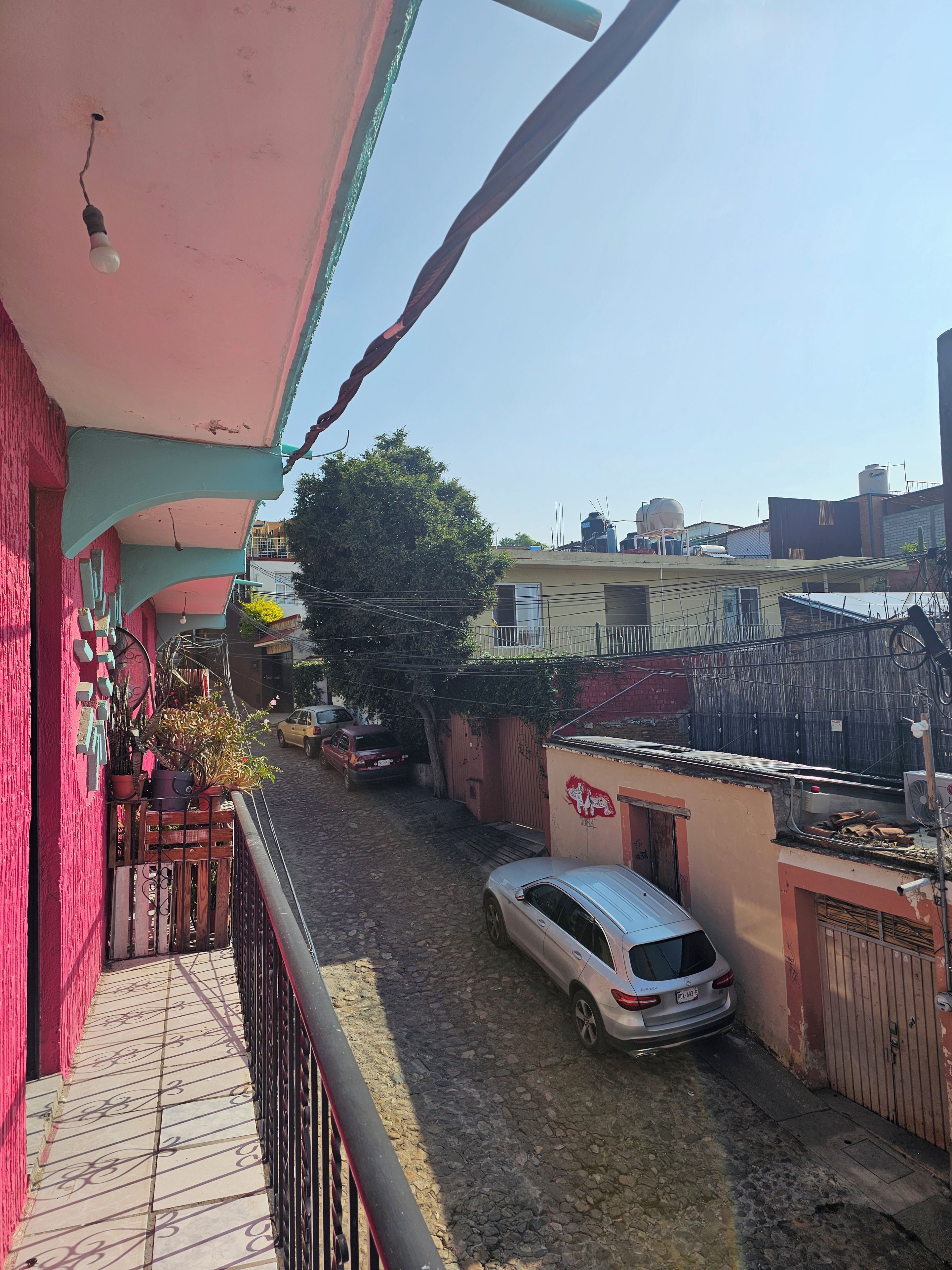 A residential area with a balcony, a parked car, and a building with a red door.