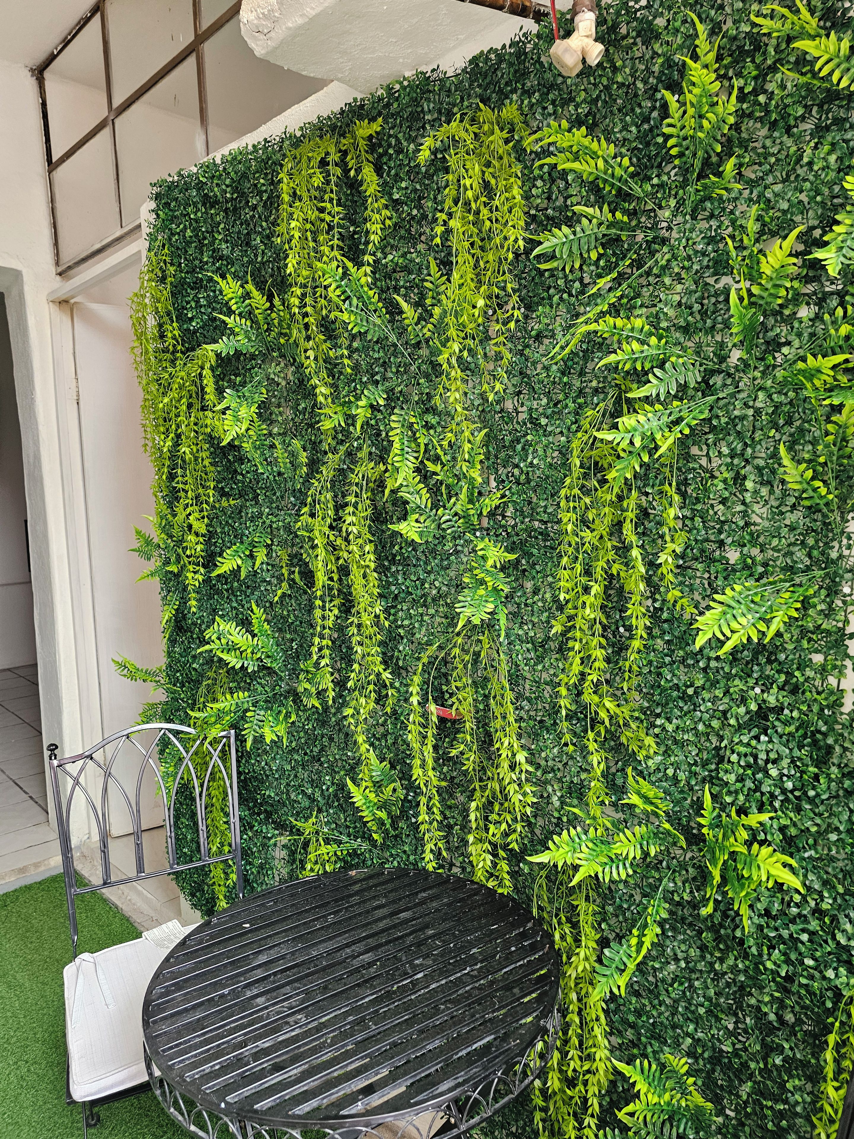 A wall with dense green foliage, a metal chair, and a white table.
