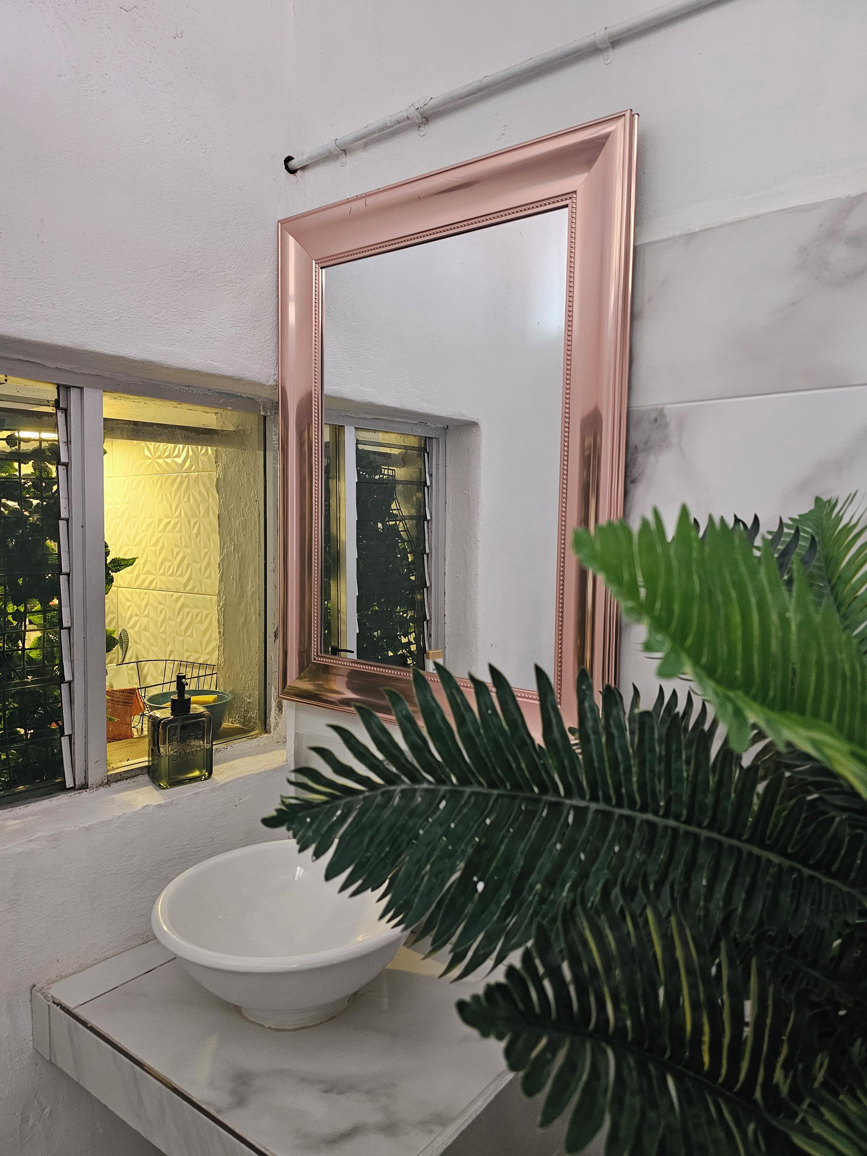 A bathroom with a white sink, a large mirror with a copper frame, and a window with a view of greenery outside.