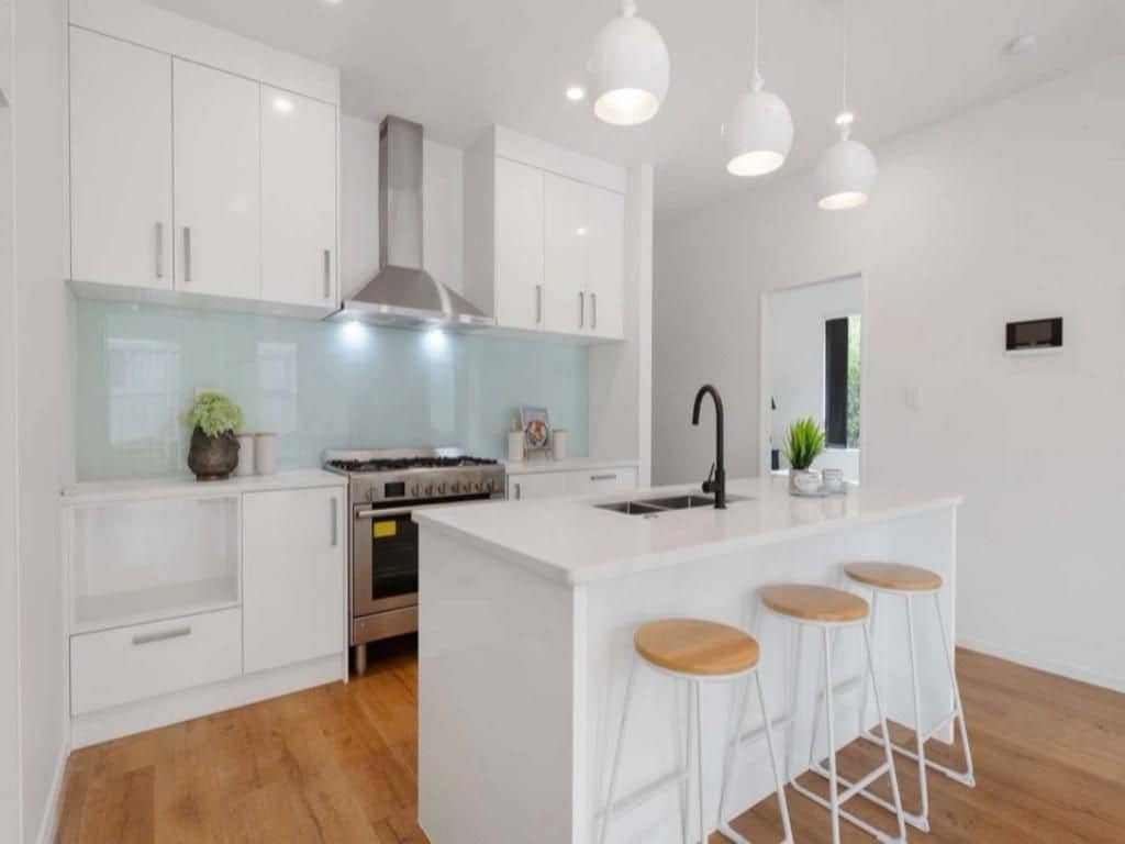 Una cocina moderna con armarios blancos, una isla central con taburetes e iluminación colgante.
