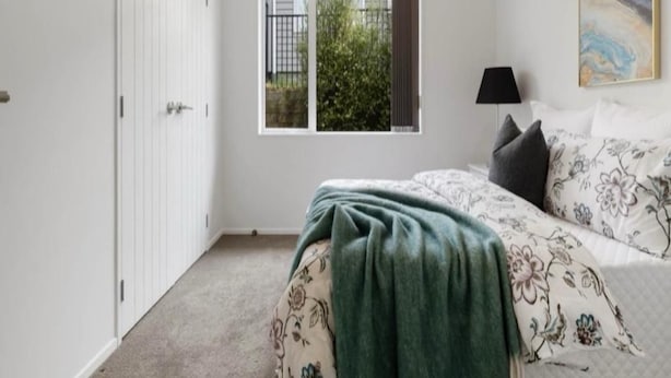 A bedroom with a bed, a window, a door, and a painting on the wall.