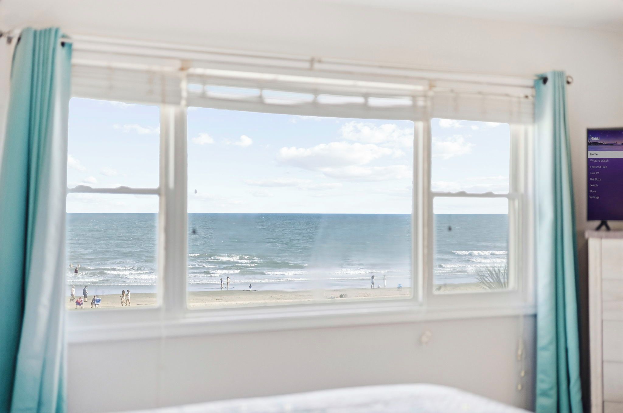 Une chambre avec une fenêtre donnant sur une plage, un lit et un écran fixé au mur qui affiche un menu.