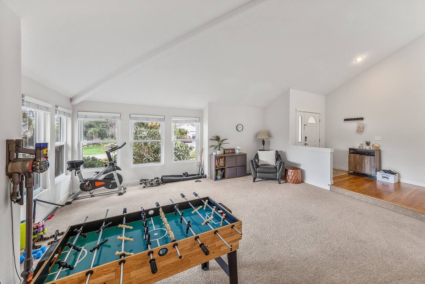 A spacious room with a foosball table, exercise equipment, and a view of greenery through large windows.