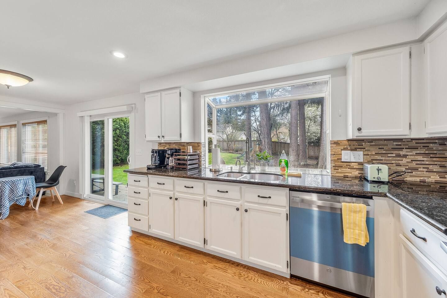 A modern kitchen with white cabinets, a granite countertop, and a large window.
