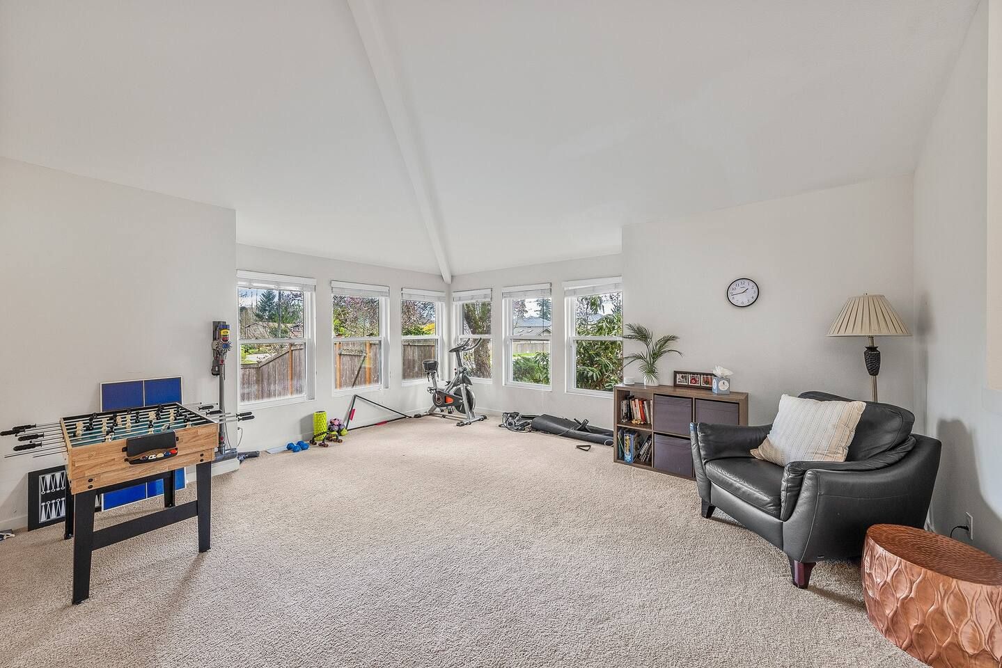 A spacious living room with a foosball table, exercise bike, and a leather sofa.