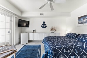 Ein Schlafzimmer mit einem Bett, einem Fernseher, einem Deckenventilator, einem Schreibtisch und einem Fenster.