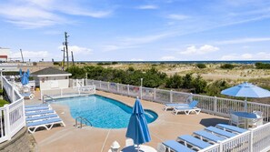 Ein Poolbereich mit Liegestühlen und Sonnenschirmen, umgeben von einem weißen Zaun, mit Blick auf einen Strand.