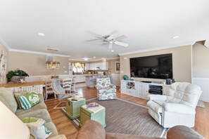 A modern living room with a large flat-screen TV, comfortable seating, and a kitchen in the background. - Spacious 4BR Wildwood Crest Home with 3 Private Decks & Garage Parking (Wildwood Crest)