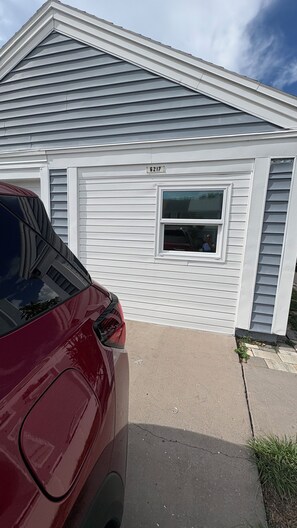 A single-story house with a garage door, a visible window, and a red vehicle parked in front. - Lovely Tiny House in Tampa Town and Country. 1 or 2 people. Excellent Location. (Tampa)