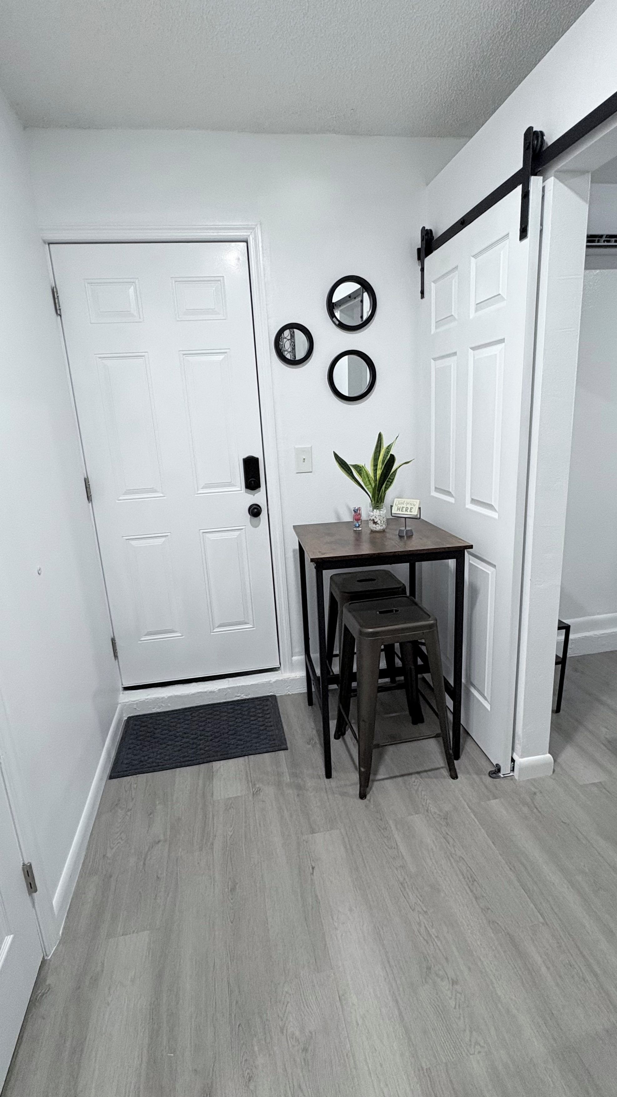 A hallway with a white door, a small table with a plant, and three wall-mounted mirrors.
