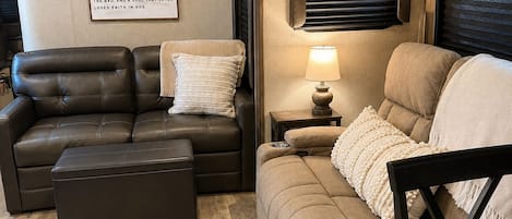 Un interior de autocaravana acogedor con un sofá de cuero marrón, un sofá beige y una pequeña mesa con una lámpara.