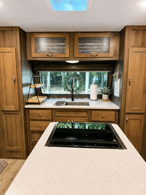 A compact kitchen with wooden cabinets, a built-in sink, and a window overlooking greenery. - Rivers Edge Retreat at River Rock Landing (Gadsden)