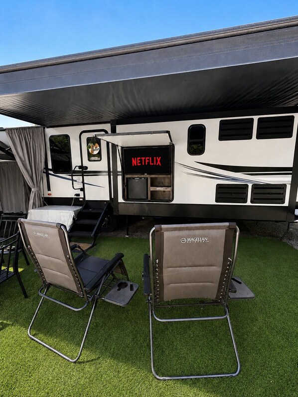 Un véhicule récréatif orné d’un logo Netflix, doté d’une petite kitchenette et de deux chaises de la marque Magellan, le tout installé sur une pelouse artificielle.