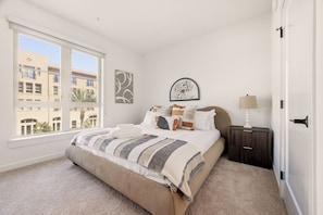 A bedroom with a large bed, a nightstand, a lamp, and two wall art pieces. - Modern King 2B2B｜Pool & Gym｜70in Smart 4K TV (Montclair)