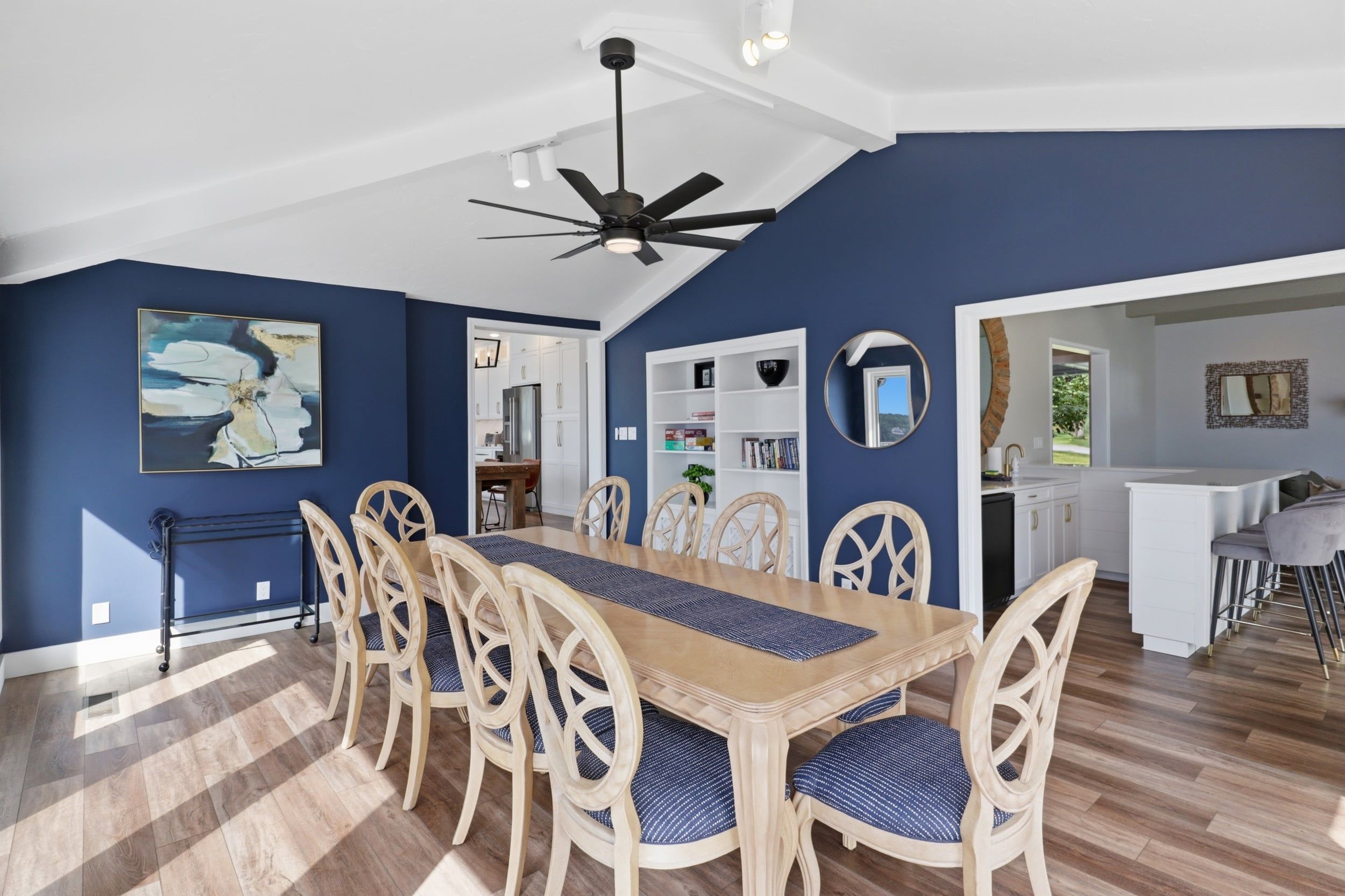 A dining area with a wooden table and chairs, a ceiling fan, and a view into the kitchen.