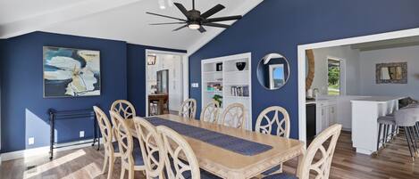 A dining area with a wooden table and chairs, a ceiling fan, and a view into the kitchen.