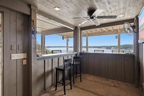 A covered outdoor area with a ceiling fan, a bar counter, and two chairs. - 7BR Lake View Escape, Hot Tub, Lake Views & Game Room (Lake Ozark)