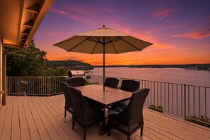 A deck with a table and chairs, overlooking a body of water with a sunset view. - 7BR Lake View Escape, Hot Tub, Lake Views & Game Room (Lake Ozark)