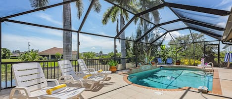 A covered outdoor area with a pool, lounge chairs, and palm trees.