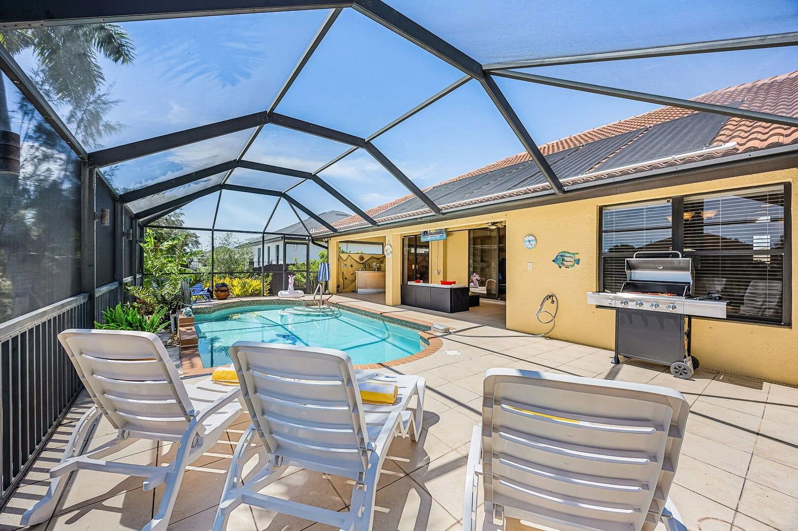 A covered outdoor area with a pool, lounge chairs, and a barbecue grill. - Canal Retreat with Heated Pool, Bikes & Waterfront Fun in Cape Coral - Villa Amarillo - Roelens (Cape Coral)