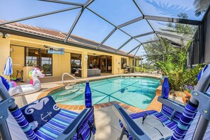 A pool area with lounge chairs, a glass-enclosed structure, and a building with a sign. - Canal Retreat with Heated Pool, Bikes & Waterfront Fun in Cape Coral - Villa Amarillo - Roelens (Cape Coral)
