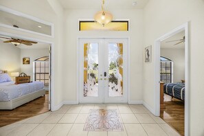 A spacious hallway with a double door featuring decorative glass panels, a patterned rug, and a ceiling fan. - Canal Retreat with Heated Pool, Bikes & Waterfront Fun in Cape Coral - Villa Amarillo - Roelens (Cape Coral)