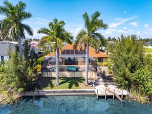 A residential property with a swimming pool, palm trees, and a covered outdoor area. - Canal Retreat with Heated Pool, Bikes & Waterfront Fun in Cape Coral - Villa Amarillo - Roelens (Cape Coral)