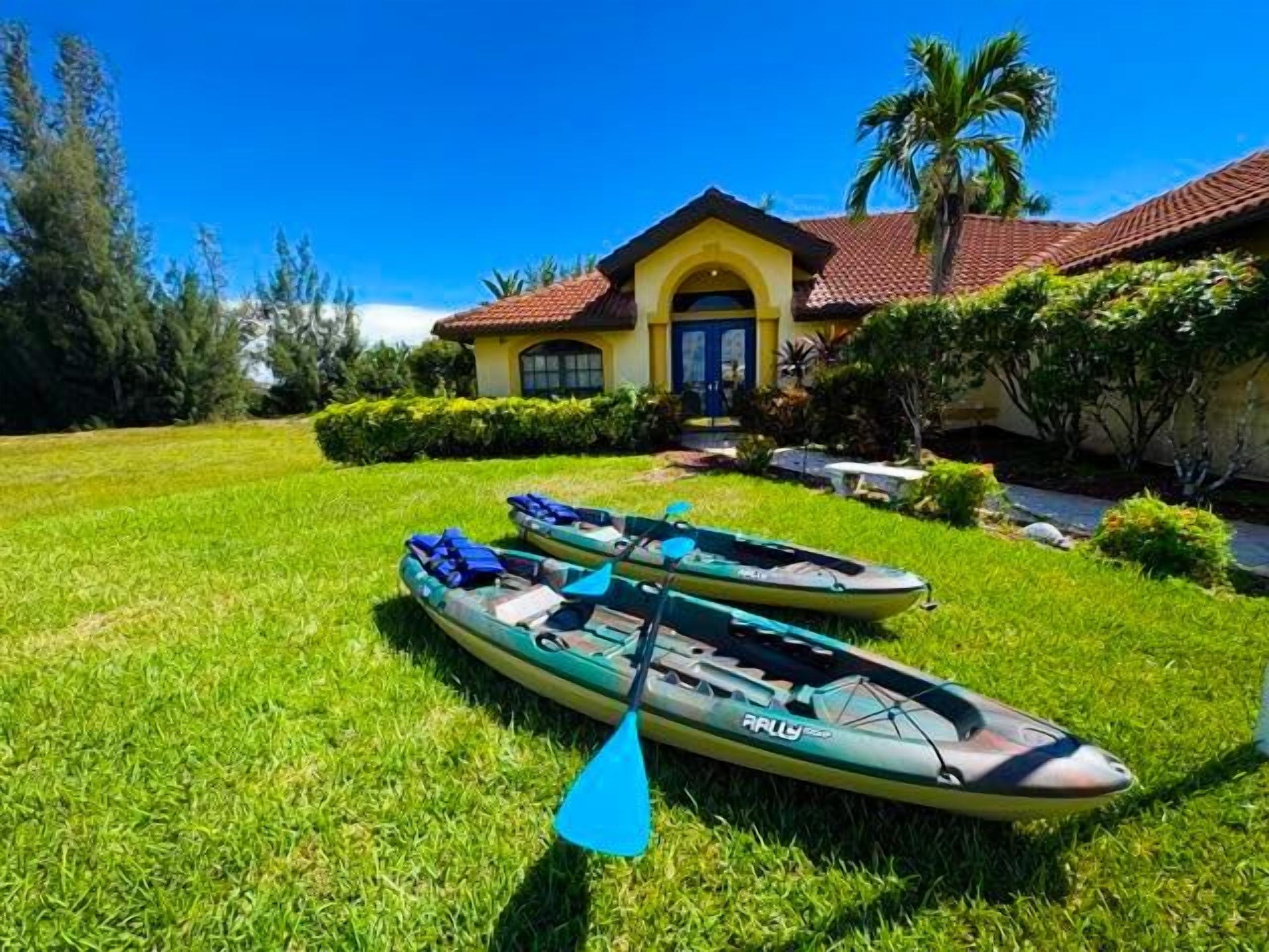 A house with a red-tiled roof, a front yard with two kayaks, and a palm tree.