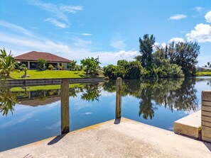 Um lago tranquilo com um píer, uma casa com telhado vermelho e vegetação exuberante.