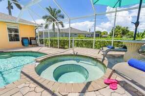 A swimming pool with a hot tub, surrounded by a covered patio area with lounge chairs and a table. - Tropical Canal Escape with Pool, Spa & Kayaks in Cape Coral - Pineapple Princess - Roelens (Cape Coral)