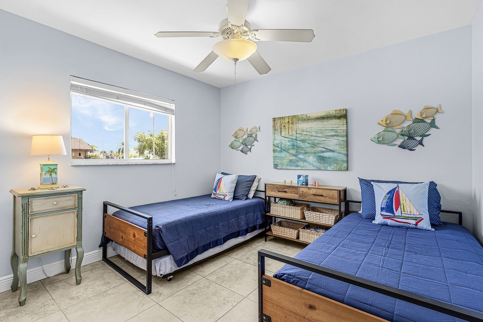 A bedroom with two beds, a ceiling fan, a window with a view, and wall art.