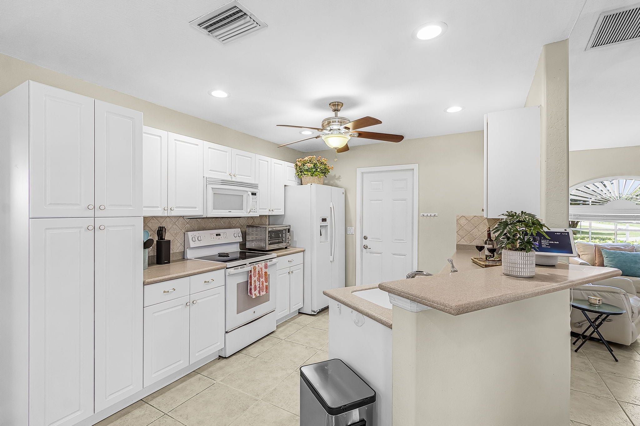 A modern kitchen with white cabinets, a microwave, oven, and a ceiling fan.