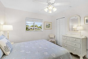 A bedroom with a bed, a dresser, a chair, a window with a view, and a ceiling fan. - Tropical Canal Escape with Pool, Spa & Kayaks in Cape Coral - Pineapple Princess - Roelens (Cape Coral)