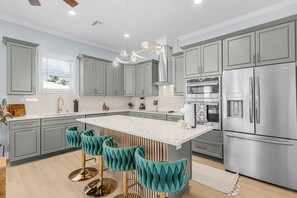 A modern kitchen with grey cabinets, a central island with bar stools, stainless steel appliances, and a decorative light fixture. - Poolside Fun, Pickleball & Coastal Adventures Await in Fort Myers - Jefferson Palms - Roelens (Fort Myers Beach)