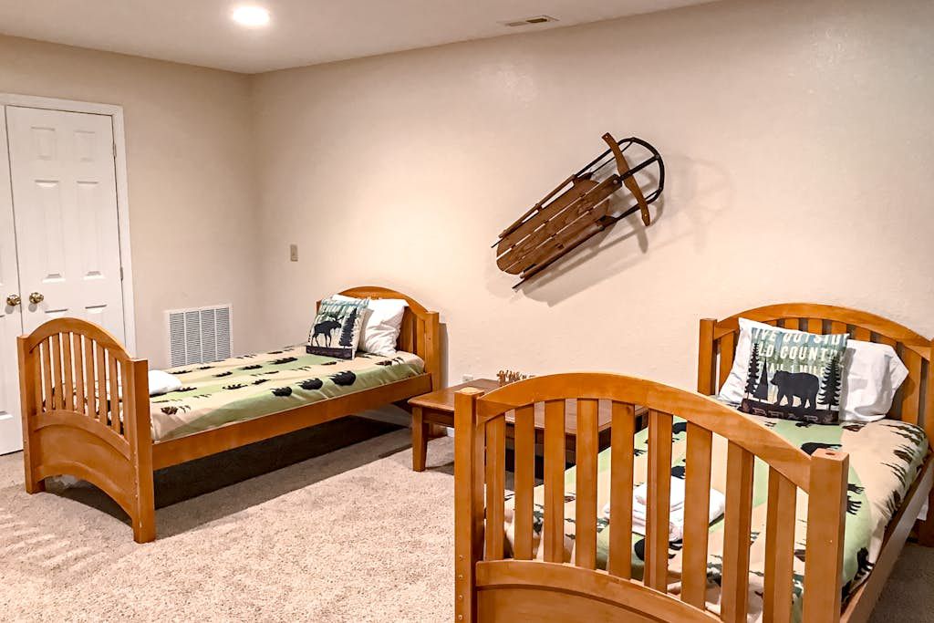 Une chambre avec deux lits en bois, une porte blanche et une luge accrochée au mur.
