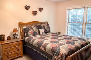 A bedroom with a wooden bed, a nightstand, and a window with blinds. - Tiger Den - Sugar Mountain, pool table, views (Banner Elk)