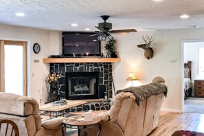 A living room with a stone fireplace, a mounted television, a ceiling fan, and a deer head decoration. - Tiger Den - Sugar Mountain, pool table, views (Banner Elk)