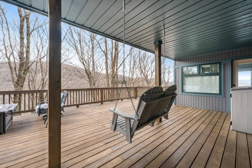 A wooden deck with a swing chair, a grill, and a window overlooking a mountainous landscape.