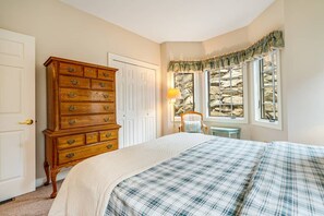 A bedroom with a large wooden dresser, a bed with a plaid bedspread, a window with a view of rocks, and a lamp on a side table. - Reserve II- long range views, fireplace, close to ski! (Banner Elk)