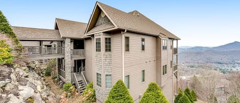 A two-story building with a stone foundation, a balcony, and a view of the surrounding landscape.
